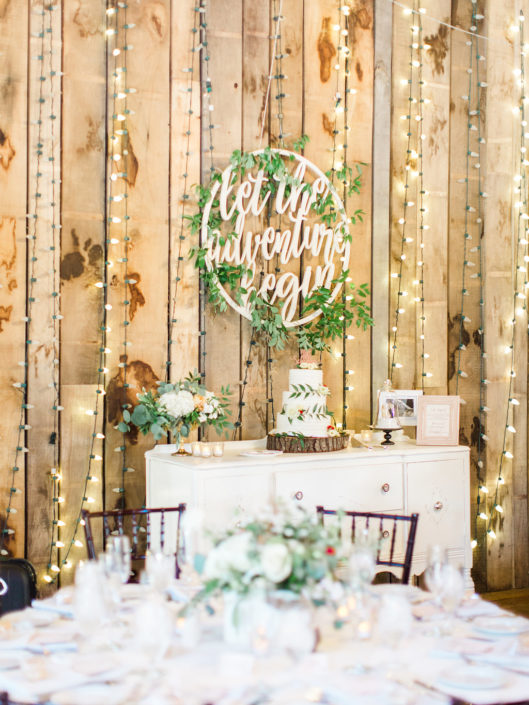 Wedding cake on decorated table with lights behind in the Pegasus Barn.