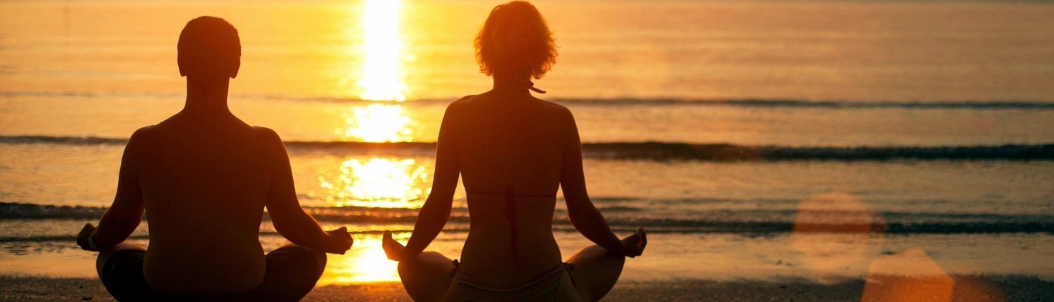 A couple doing yoga during sunset.