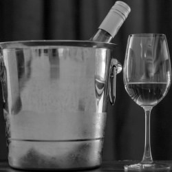 Bottle of wine in ice bucket with a glass of wine.