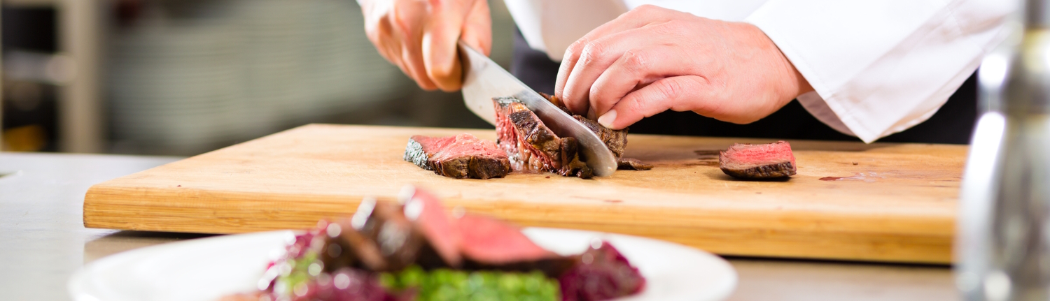 Chef slicing beef in the kitchen.