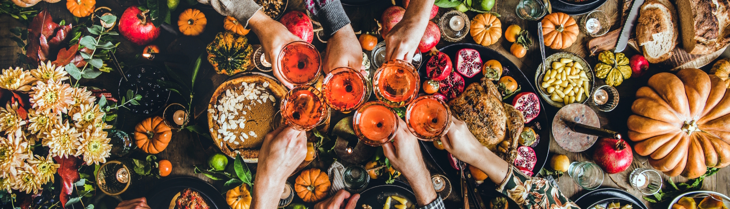 People clinking wine glasses over a table with a Thanksgiving feast.