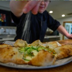 Chef seasoning a specialty pizza up close.