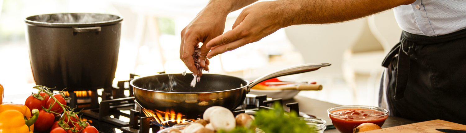 Chef putting vegetables in a sauté pan.