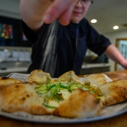 Chef adding seasoning to a wood-fired pizza.